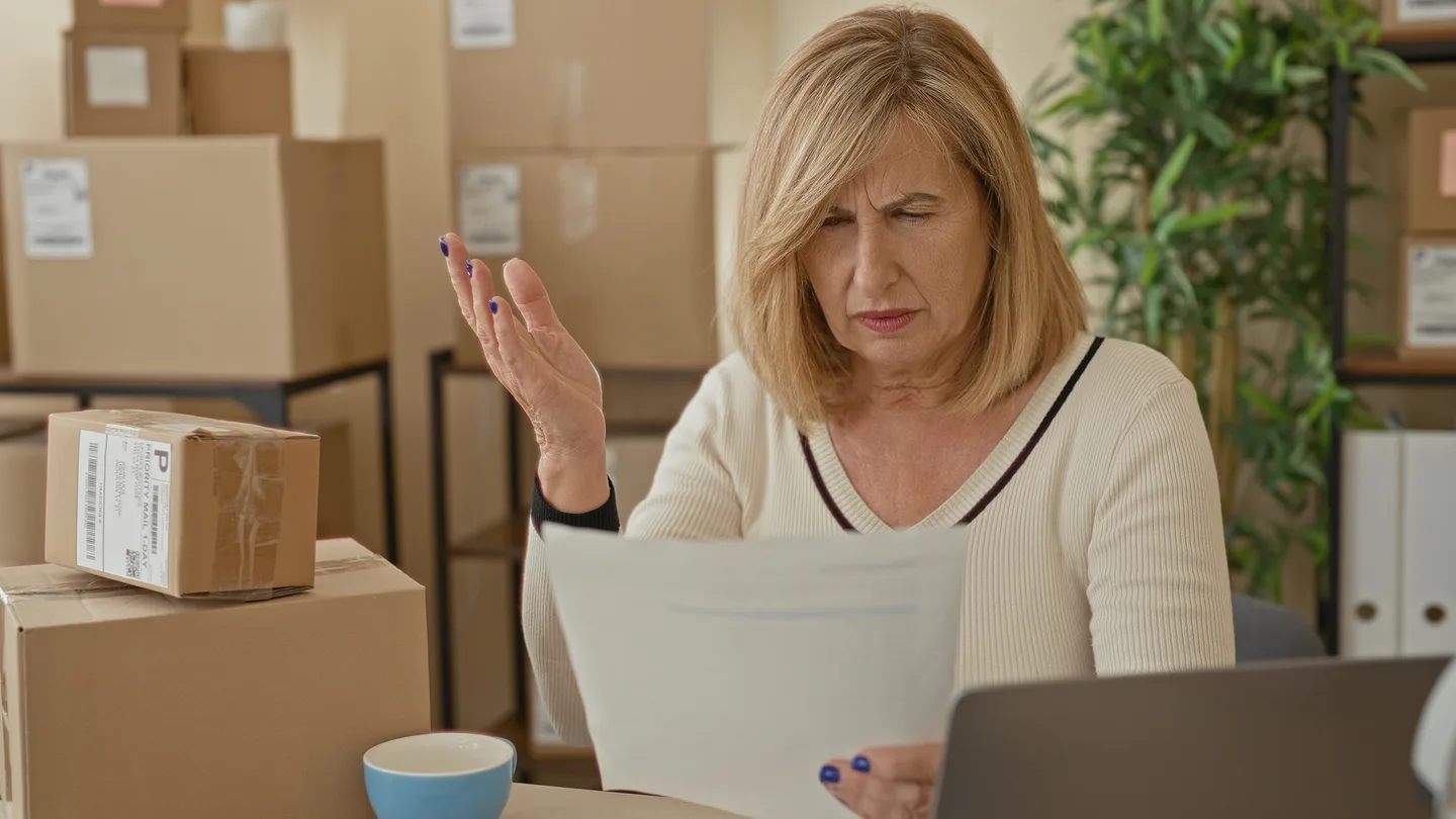 A business owner reviewing paperwork beside a laptop and stacked parcels